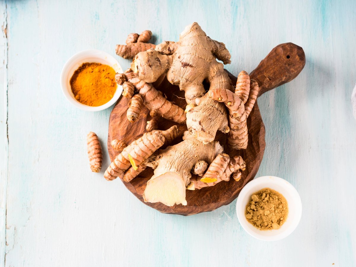 Turmeric spice and ginger in powder and roots on wooden board over blue background. Natural healthy remedy