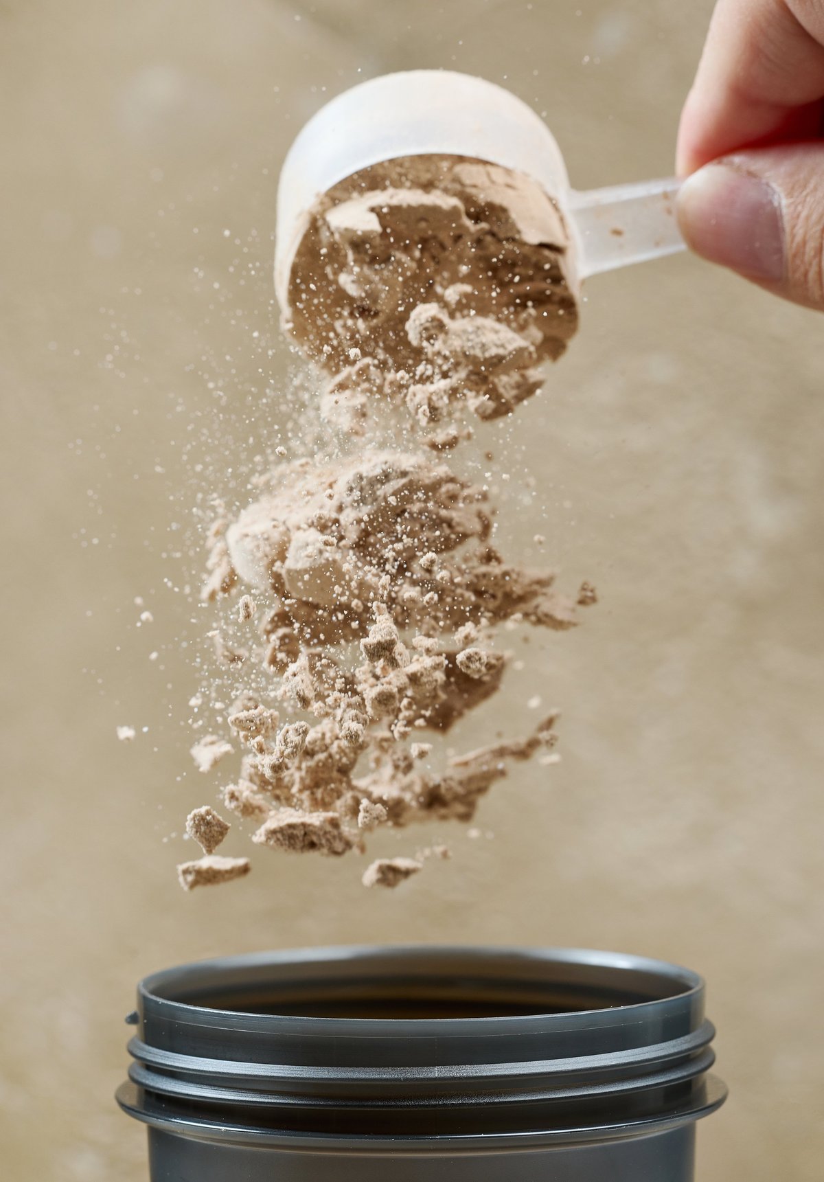 Protein powder spills in cup from measure scoop. Whey sports nutrition.