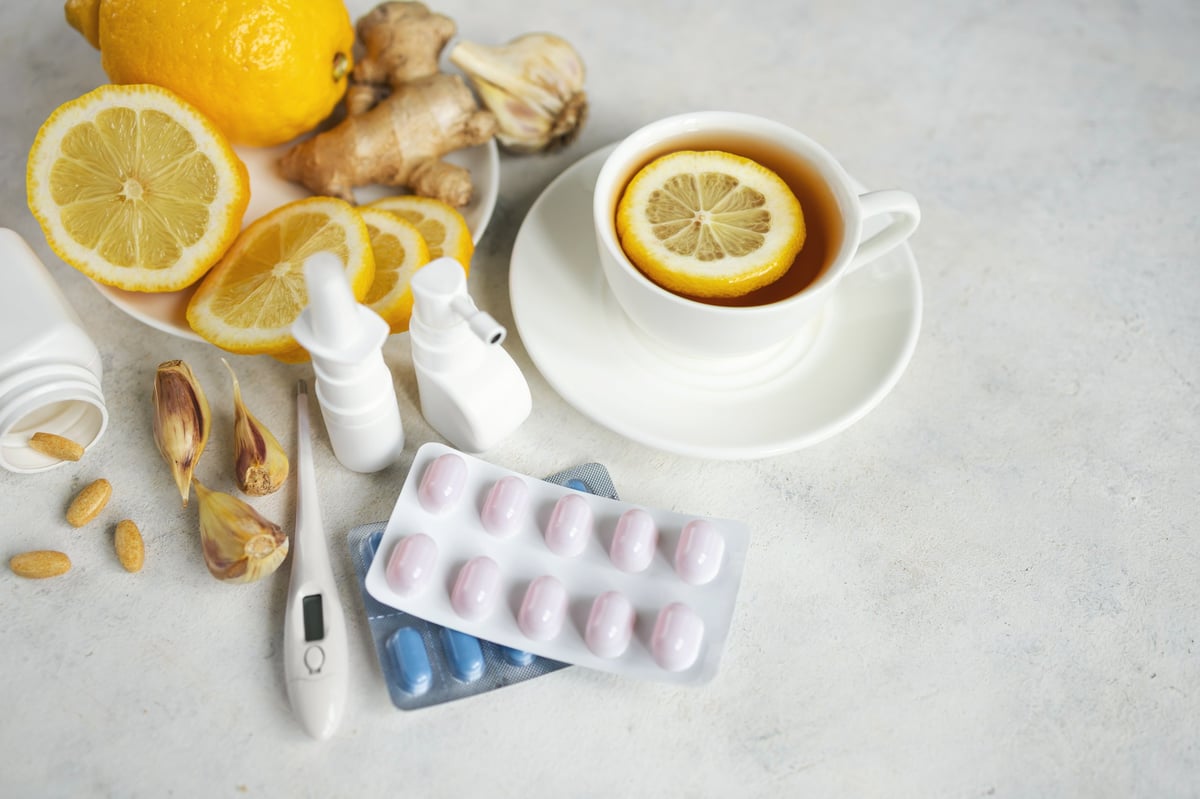 Cold and flu season treatment still life with cup of tea, lemon, pills, thermometer, nasal sprays, garlic and ginger, health and wellness concept.