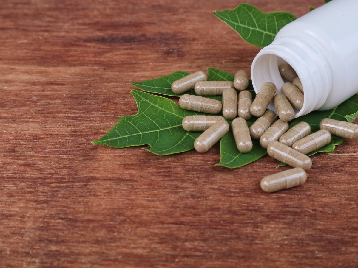 Herbal medicine capsules spilled on green leaves over wooden background. Perfect for natural health, alternative medicine, and organic wellness concept