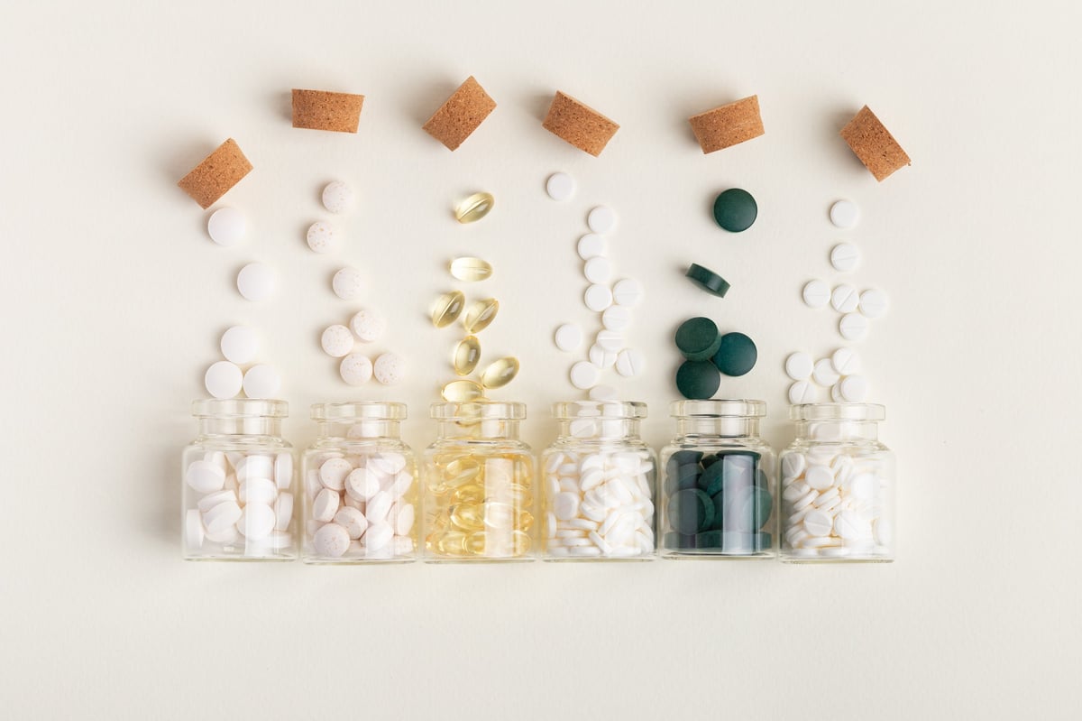Small glass jars filled with vitamins, minerals, and food supplements from above on beige background.
