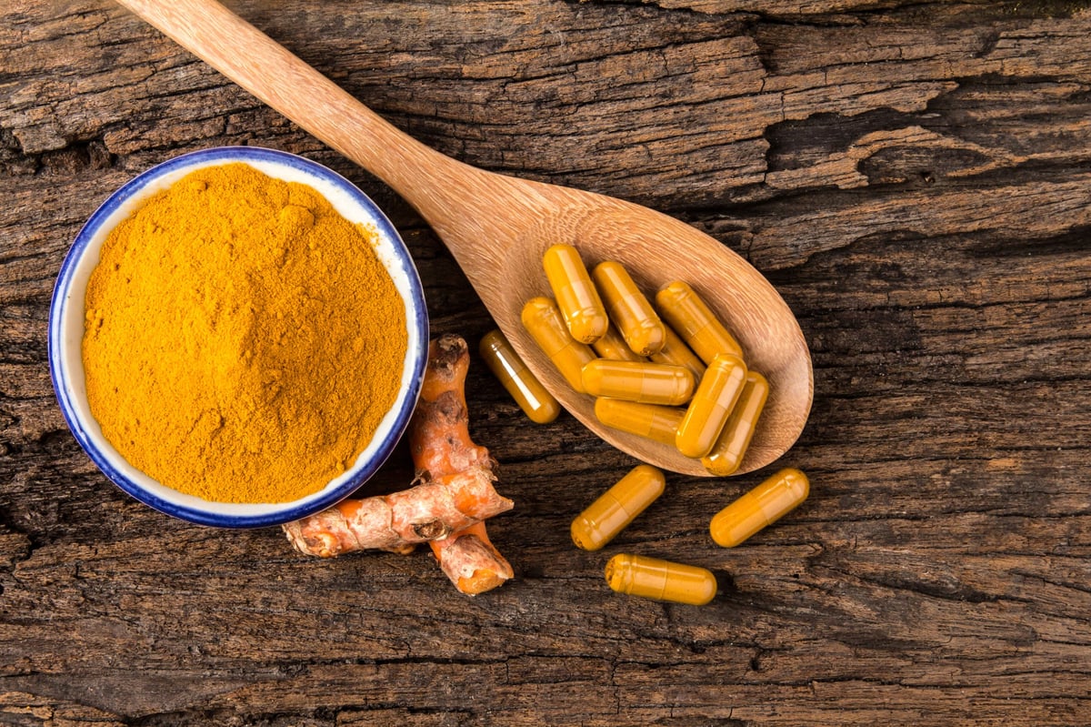 The turmeric powder, capsule and roots curcumin on wooden plate